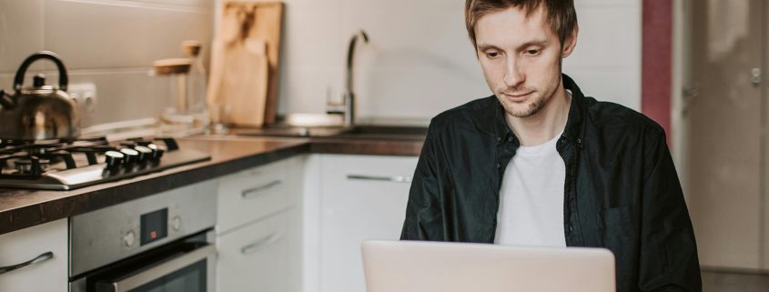 KinseyInvestigations.com Integrity Checks - A man works on a laptop at a kitchen table.