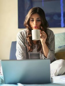 KinseyInvestigaitons.com Mystery Shopper Investigations - A woman holding a mug sits in bed with a laptop.