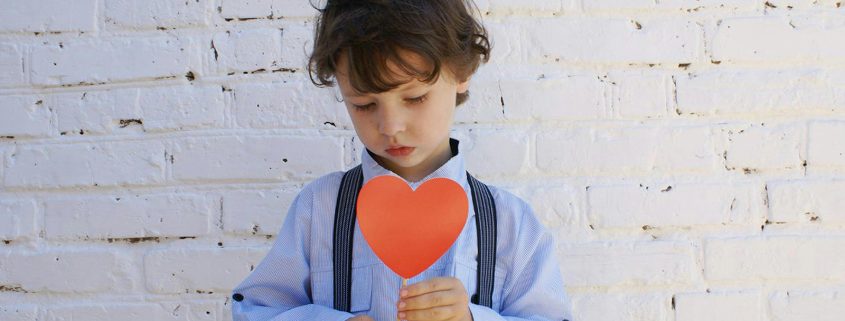 KinseyInvestigations.com Child Custody - A young boy holds a paper heart in front of his chest.