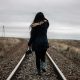 KinseyInvestigations.com Finding Missing Persons - A woman wearing a long jacket walks on a railroad track in a deserted landscape.