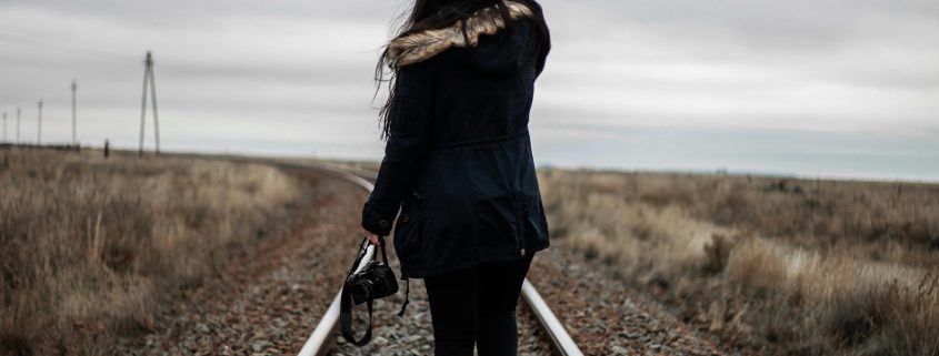 KinseyInvestigations.com Finding Missing Persons - A woman wearing a long jacket walks on a railroad track in a deserted landscape.