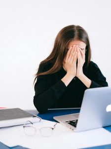 KinseyInvestigations.com Internet Catfishing - A woman sitting in front of a laptop covers her face with her hands.