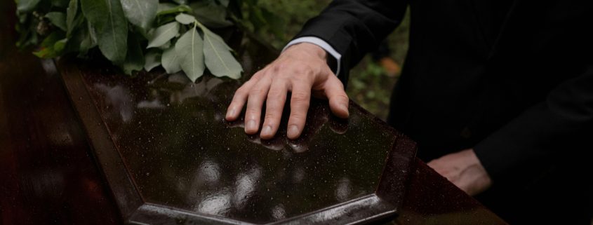 KinseyInvestigations.com Wrongful Death Investigations - A mourner rests their hand on a casket.