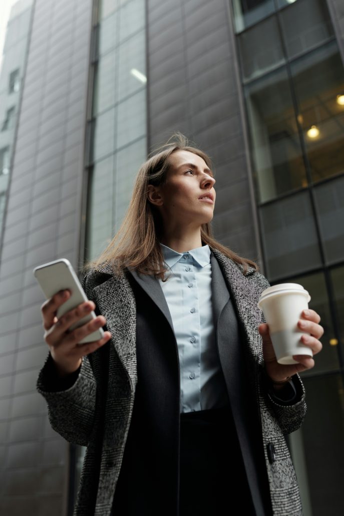 Woman in business attire with a cell phone in one hand and a cup of coffee in the other - Visit KinseyInvestigations.com. 