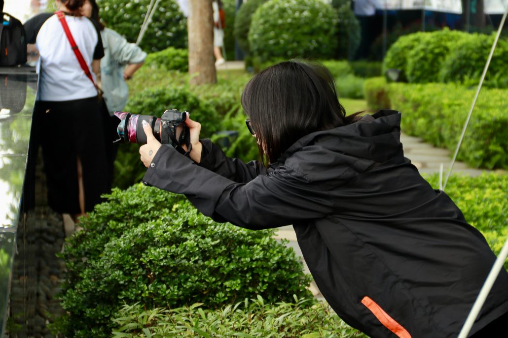 Female photographer in a dark coat photographing people from behind - Visit KinseyInvestigations.com. 