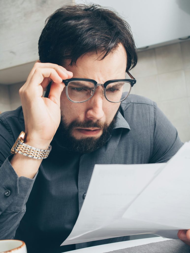 A dark-haired man in glasses looks shocked as he reads something on a sheet of paper - Visit KinseyInvestigations.com. 