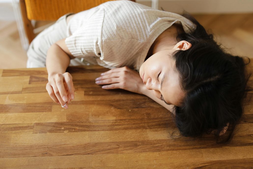 Woman with long dark hair with her head down on a table as she removes her wedding ring - Visit KinseyInvestigations.com. 