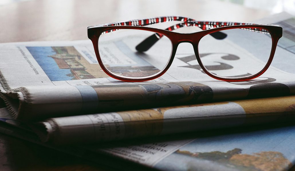 A pair of glasses sitting on top of a stack of magazines - Visit KinseyInvestigations.com. 