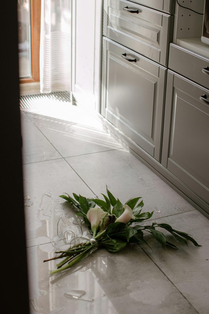 A broken vase with lilies on a white tile floor - Visit KinseyInvestigations.com. 