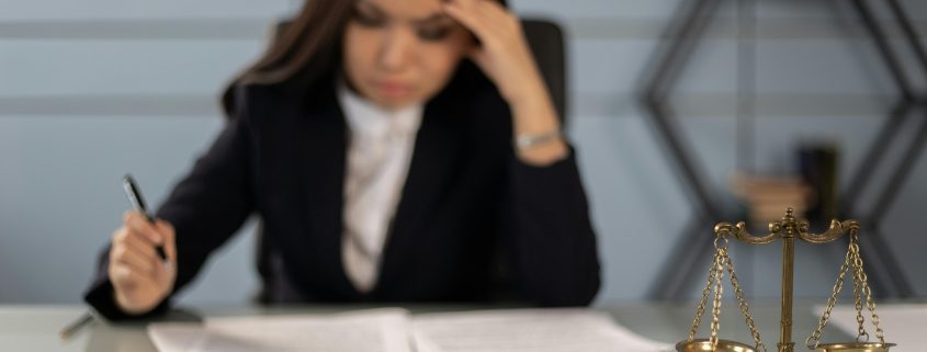 Professional woman blurred in background looking over papers, focus on scales of justice in foreground - Consult KinseyInvestigations.com.