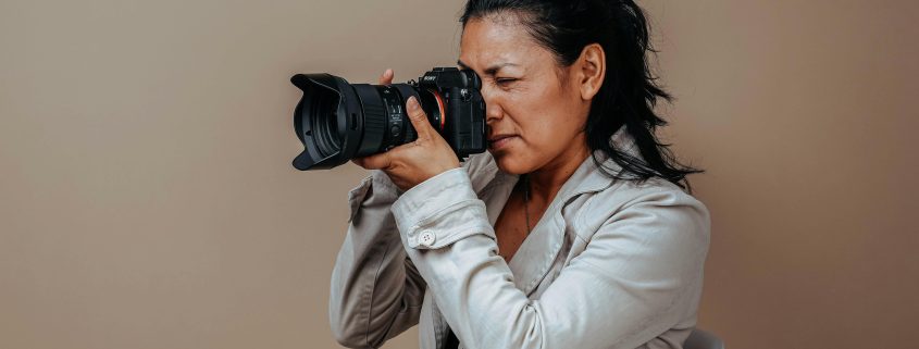 Woman in gray suit holding DSLR camera to her eye - Visit KinseyInvestigations.com.