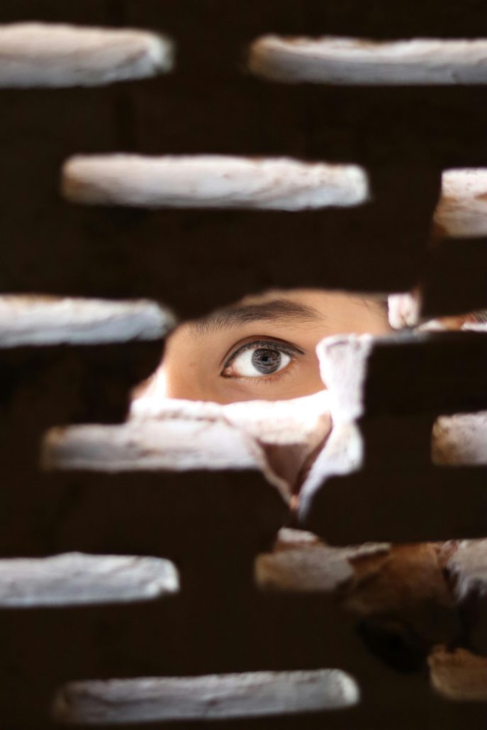 A woman's eye peeking through a brick wall - Visit KinseyInvestigations.com. 