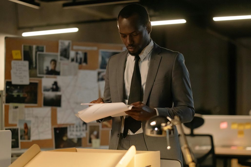 Black male detective in front of board displaying evidence - Visit KinseyInvestigations.com. 