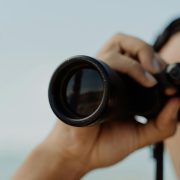 Cropped photo of one lens of a pair of binoculars in a woman's hands - Visit KinseyInvestigations.com.