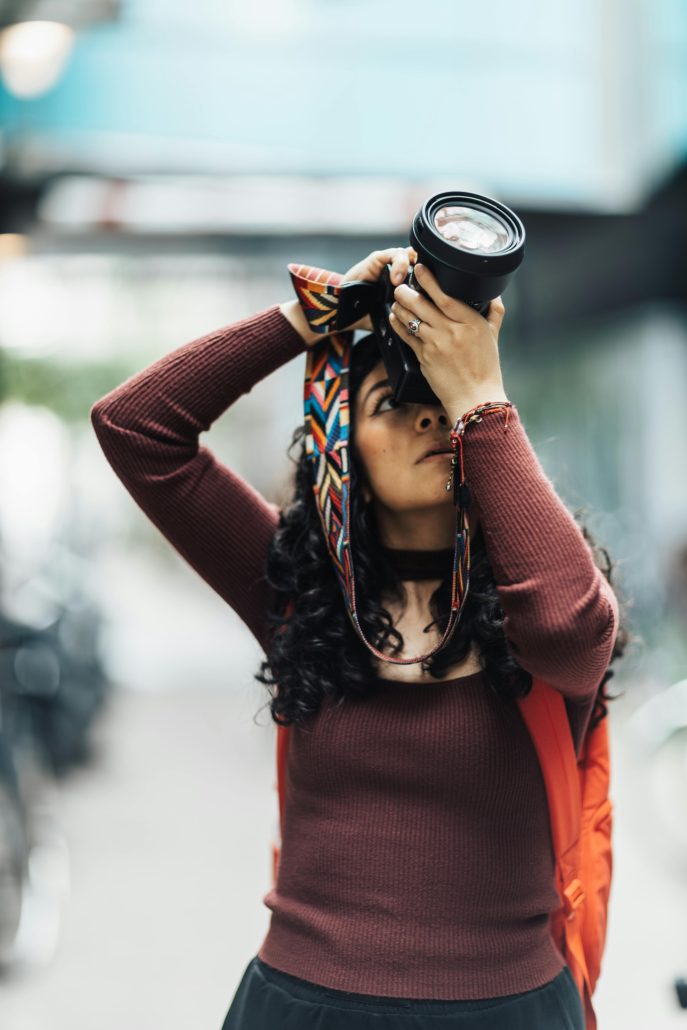 A woman raising a camera to photograph something above her head - Visit KinseyInvestigations.com.