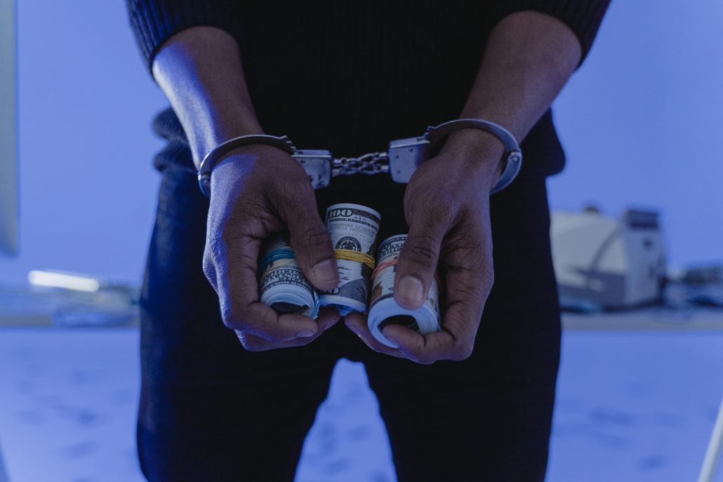 A man's hands in handcuffs holding rolls of cash - Visit KinseyInvestigations.com. 