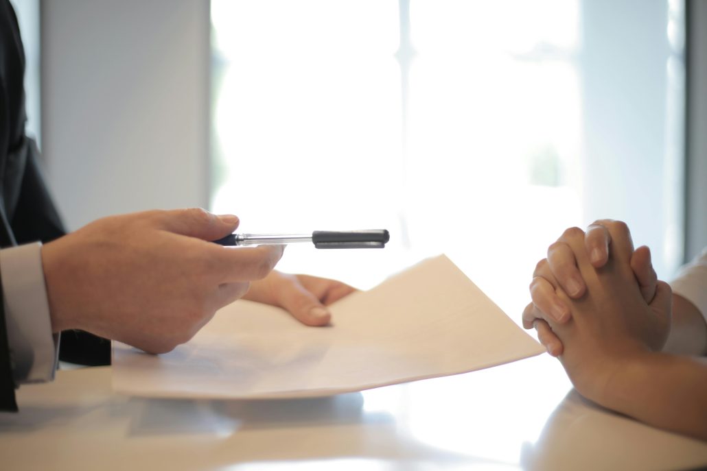 Two pairs of hands across from each other. The left hands are holding documents and offering a pen. - Visit KinseyInvestigations.com. 