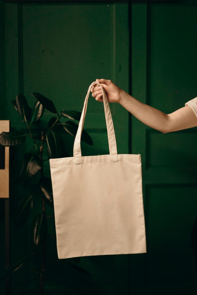 A shopper holding up a reusable linen shopping bag against a green background - Consult KinseyInvestigations.com. 