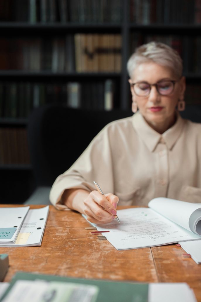 A mature woman with gray hair and glasses reviewing a file - Consult KinseyInvestigations.com. 