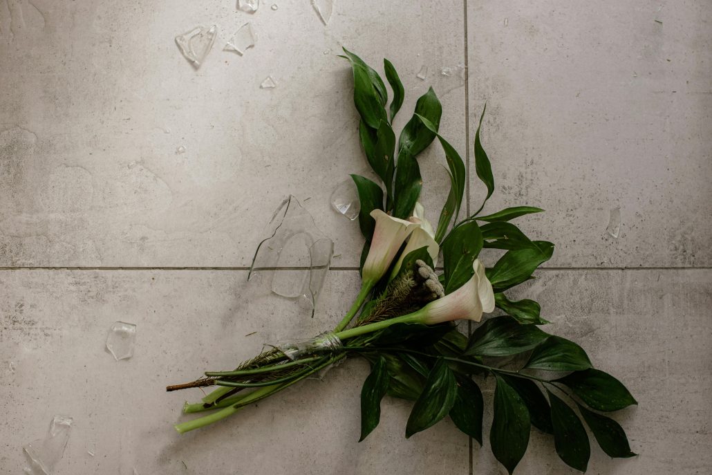 Calla lilies in a broken vase on the floor - Visit KinseyInvestigations.com.