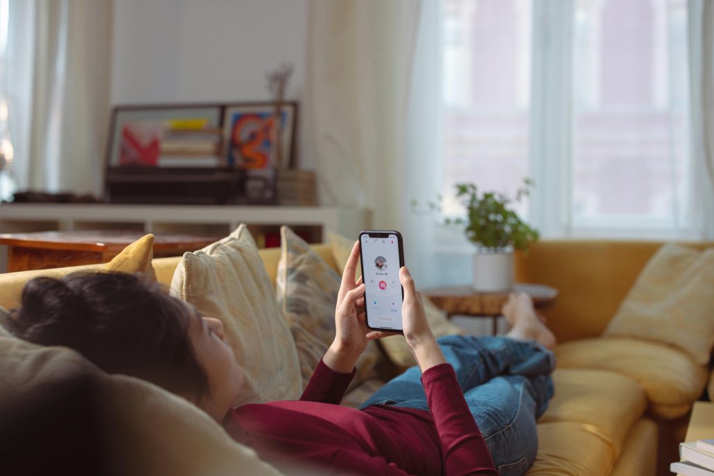 A woman lying down on her couch checking a social media notification - Visit KinseyInvestigations.com. 